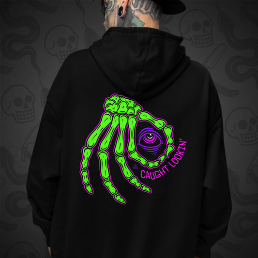 Cropped image of a Model wearing a black zippered hoodie with Caught Lookin' design printed on the back with vibrant colors.