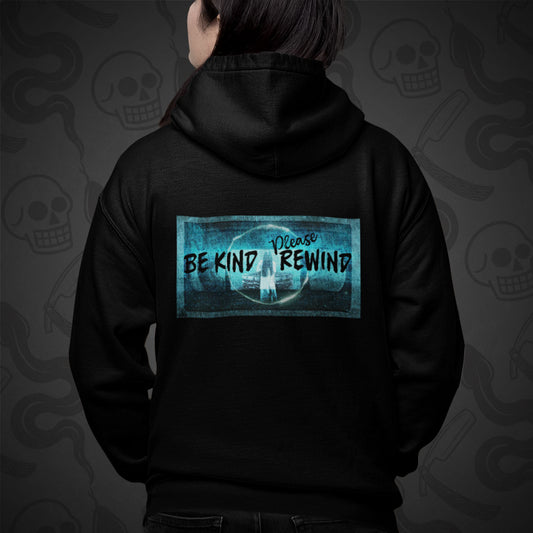 Cropped image of a Model wearing zippered hoodie with the Be Kind Please Rewind design printed on the back with vibrant colors on a patterned monochromatic background.